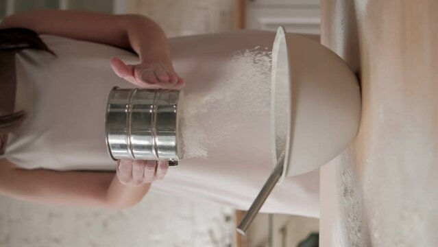 Woman is sifting flour through a metal sifter, hand closeup view. Preparing flour for baking cake in kitchen at home. Prepares dough for baking pizza bread, process of sifting flour in the bakery shop