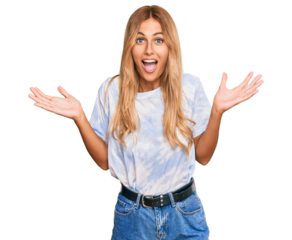 Beautiful blonde young woman wearing casual tie dye shirt celebrating victory with happy smile and winner expression with raised hands