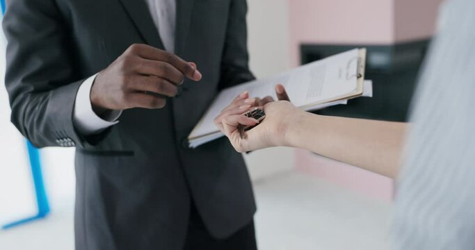 With excitement in the air, a blonde woman real estate agent presents the key to a new house to a beaming African couple, surrounded by their celebration home-buying process.
