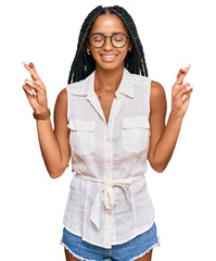 Beautiful hispanic woman wearing casual clothes and glasses gesturing finger crossed smiling with...