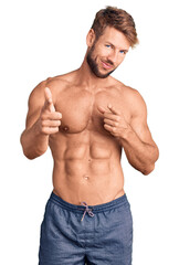 Fototapeta premium Young caucasian man standing shirtless pointing fingers to camera with happy and funny face. good energy and vibes.
