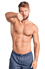 Young caucasian man standing shirtless looking unhappy and angry showing rejection and negative with thumbs down gesture. bad expression.