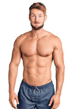 Young caucasian man standing shirtless puffing cheeks with funny face. mouth inflated with air, crazy expression.