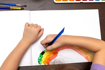 Child draws paints on a paper. Children's hands in kindergarten painting hearts with temperas and a brush on a sheet of paper. Initial education of children. Kid in art class