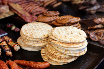 Pita bread nearby on grilled sousage and different tipe of meat on grill.