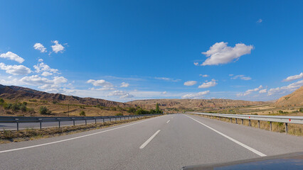 View from the car onto an empty tarmac road. Beautiful mountains ahead. Clouds in the blue sky. Road trip.