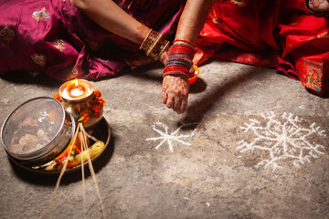 Two Indian women are making an Auspicious Hindu design pattern (rangoli) for the Karwa Chauth...