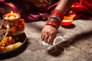 An Indian woman is making an Auspicious Hindu design pattern (rangoli) for the Karwa Chauth...