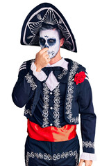 Young man wearing day of the dead costume over background smelling something stinky and disgusting, intolerable smell, holding breath with fingers on nose. bad smell