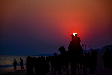 Silhouette of beach life Scene on a clear dusk with orange Sun behind a couple at renowned Indian...