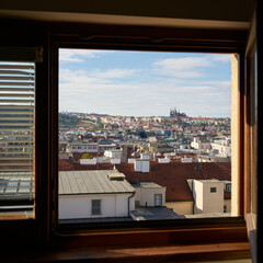 Blick durch ein geöffnetes Fenster über die Altstadt von Prag zur Prager Burg