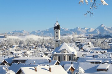Blick auf das tief verschneite Nesselwang mit der Pfarrkirche St. Andreas, im Hintergrund die...