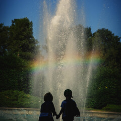Silhouettes brother and sister, on background of rainbow in fountain. Concept happy family.