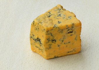 Piece of Shropshire blue cheese (veining by Penicillium roqueforti, orange color from annatto) on pale wooden cutting board