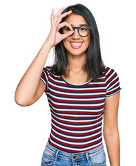 Beautiful asian young woman wearing casual clothes and glasses doing ok gesture with hand smiling, eye looking through fingers with happy face.
