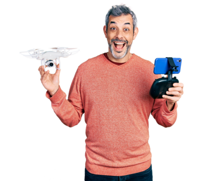 Middle age hispanic man with grey hair using drone with remote control celebrating crazy and amazed for success with open eyes screaming excited.