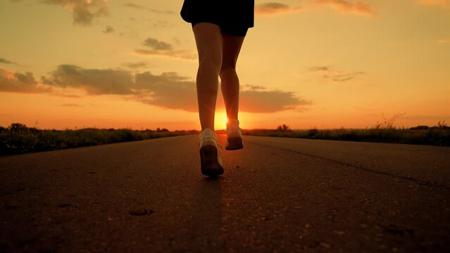 Athletes legs run along asphalt at dawn, closeup. Doing fitness, jogging on road in sun. Training jogging. Jogger girl breathes fresh air in nature. Woman runs in summer park, sunset. Jogging outside