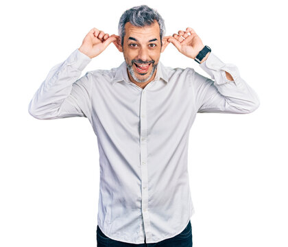 Middle age hispanic with grey hair wearing casual white shirt smiling pulling ears with fingers, funny gesture. audition problem