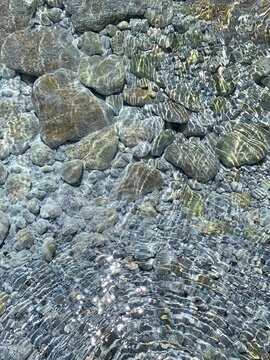 Clear sea water ripples transarent surface stones and pebbles in the seabed.