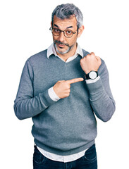 Middle age hispanic with grey hair wearing glasses in hurry pointing to watch time, impatience,...