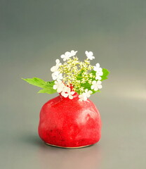 Art of flower arrangement. White composition in a red vase on a gray background. Still life with clay pomegranate. Japanese ikebana.