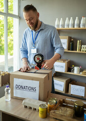 Male warehouse worker volunteer packing donations box sealing package in shipping delivery...