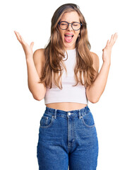 Obraz na płótnie Canvas Beautiful caucasian young woman wearing casual clothes and glasses celebrating mad and crazy for success with arms raised and closed eyes screaming excited. winner concept