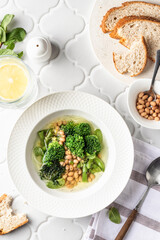 Vegetarian minestrone soup with green vegetables and beans served in white plate on white tile...