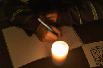 A child writes in a notebook by candlelight. Power outage due to war in Ukraine