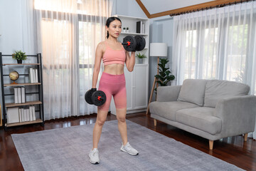 Fototapeta na wymiar Vigorous energetic woman doing dumbbell weight lifting exercise at home. Young athletic asian woman strength and endurance training session as home workout routine.