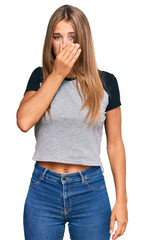 Young blonde woman wearing casual clothes smelling something stinky and disgusting, intolerable smell, holding breath with fingers on nose. bad smell