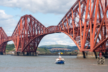 A small ferry boat next to the Forth Bridge in Queensberry