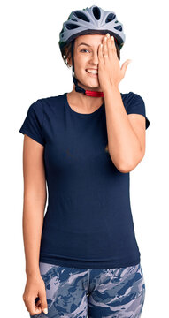 Beautiful caucasian woman wearing bike helmet covering one eye with hand, confident smile on face and surprise emotion.