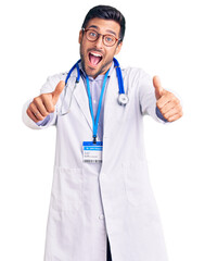 Young hispanic man wearing doctor uniform and stethoscope approving doing positive gesture with hand, thumbs up smiling and happy for success. winner gesture.