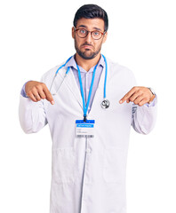 Young hispanic man wearing doctor uniform and stethoscope pointing down looking sad and upset,...