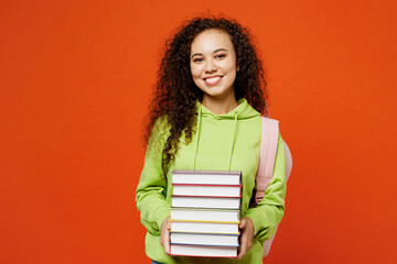 Young smiling happy teen girl student of African American ethnicity wear casual clothes backpack bag hold stack of books isolated on plain orange red background High school university college concept