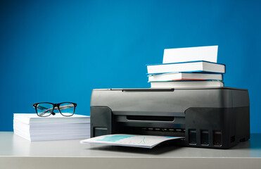 Laser printer on desk against blue background.