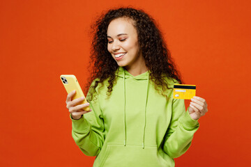 Young smiling happy woman she wear green hoody casual clothes using mobile cell phone hold credit...