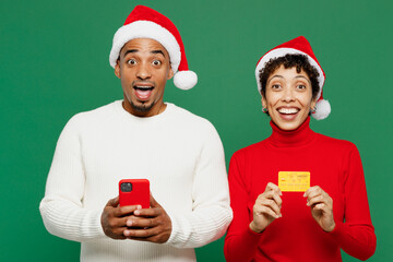 Merry young couple friend man woman in red casual clothes Santa hat posing use mobile cell phone...
