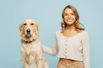 Young smiling happy cheerful owner woman with her best friend retriever hug dog wear casual clothes looking camera isolated on plain pastel light blue background studio. Take care about pet concept.