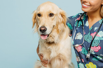 Close up cropped young happy veterinarian woman she wear uniform stethoscope heal exam hug cuddle embrace retriever dog isolated on plain pastel light blue background studio. Pet health care concept.