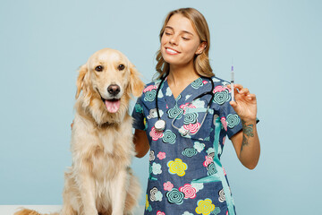 Young veterinarian woman she wear uniform stethoscope heal exam hug embrace retriever dog do vaccine injection isolated on plain pastel light blue background studio portrait. Pet health care concept.