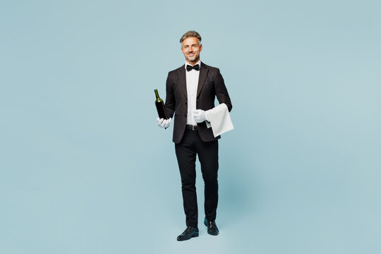 Full body adult sommelier barista male waiter butler man wears shirt black suit bow tie uniform hold in hand bottle of wine work at cafe isolated on plain blue background. Restaurant employee concept.