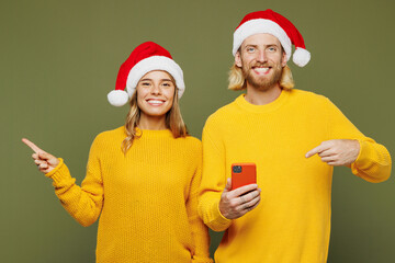 Merry young fun couple two friend man woman wears sweater Santa hat posing hold use point aside on...