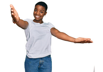 Young african american woman wearing casual white t shirt looking at the camera smiling with open arms for hug. cheerful expression embracing happiness.