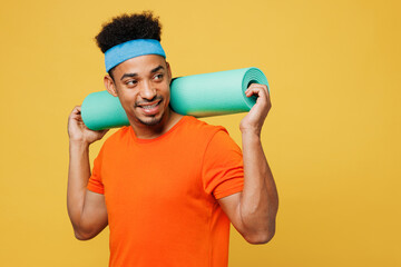 Young fitness trainer instructor sporty man sportsman wears orange t-shirt hold yoga mat look aside...