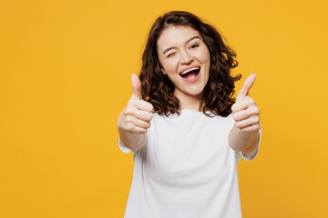 Young smiling happy cheerful Caucasian fun woman she wear white blank t-shirt casual clothes showing thumb up like gesture wink blink eye isolated on plain yellow orange background. Lifestyle concept. - obrazy, fototapety, plakaty