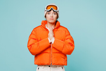 Skier young woman wears padded windbreaker jacket hat ski goggles mask hold hands folded in prayer gesture beg travel rest spend weekend winter season in mountains isolated on plain blue background. - obrazy, fototapety, plakaty