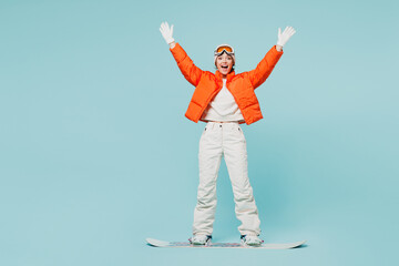 Full body young happy woman wear warm padded windbreaker jacket hat ski goggles mask snowboarding raise up hand travel rest spend weekend winter season in mountains isolated on plain blue background - obrazy, fototapety, plakaty