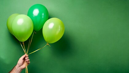 stylish birthday party or holidays with balloons three green balloons on the green background with copy space for text hand holding three bright colorful balloons indoor greeting background